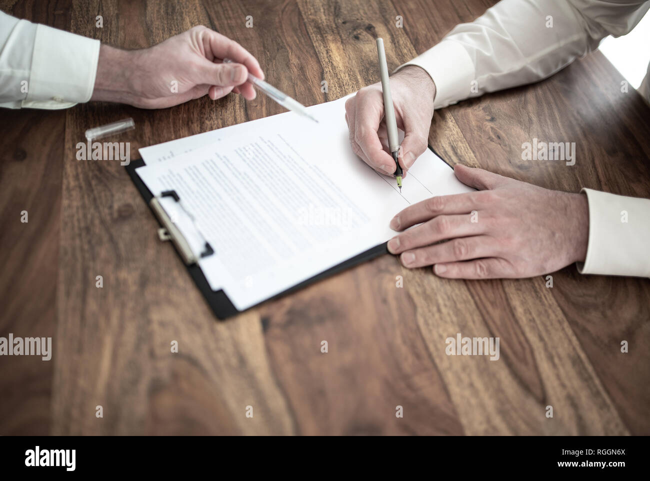 L'uomo firma il contratto alla scrivania in legno con altra persona puntando al documento Foto Stock
