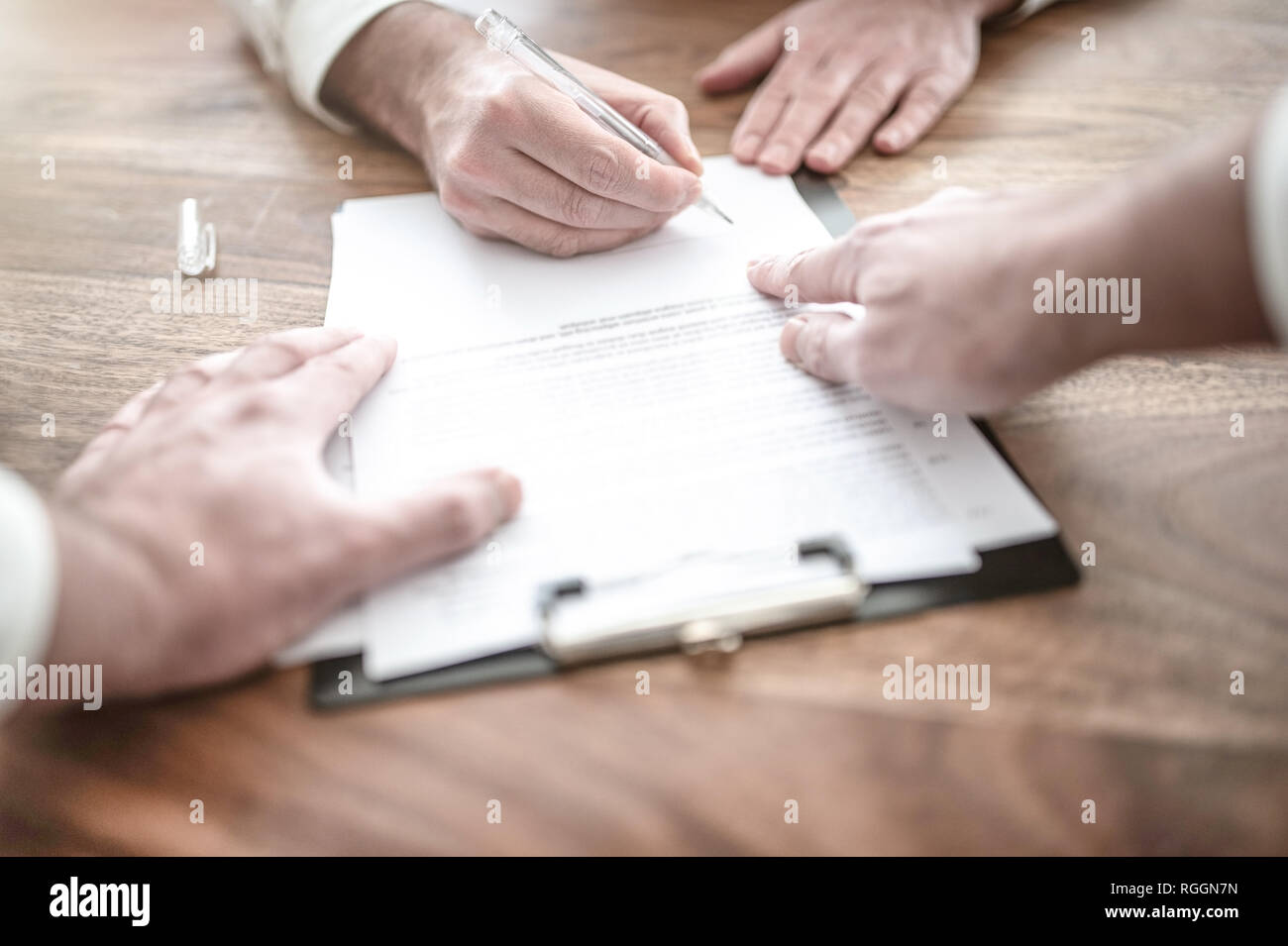 L'uomo firma il contratto alla scrivania in legno con altra persona puntando al documento Foto Stock