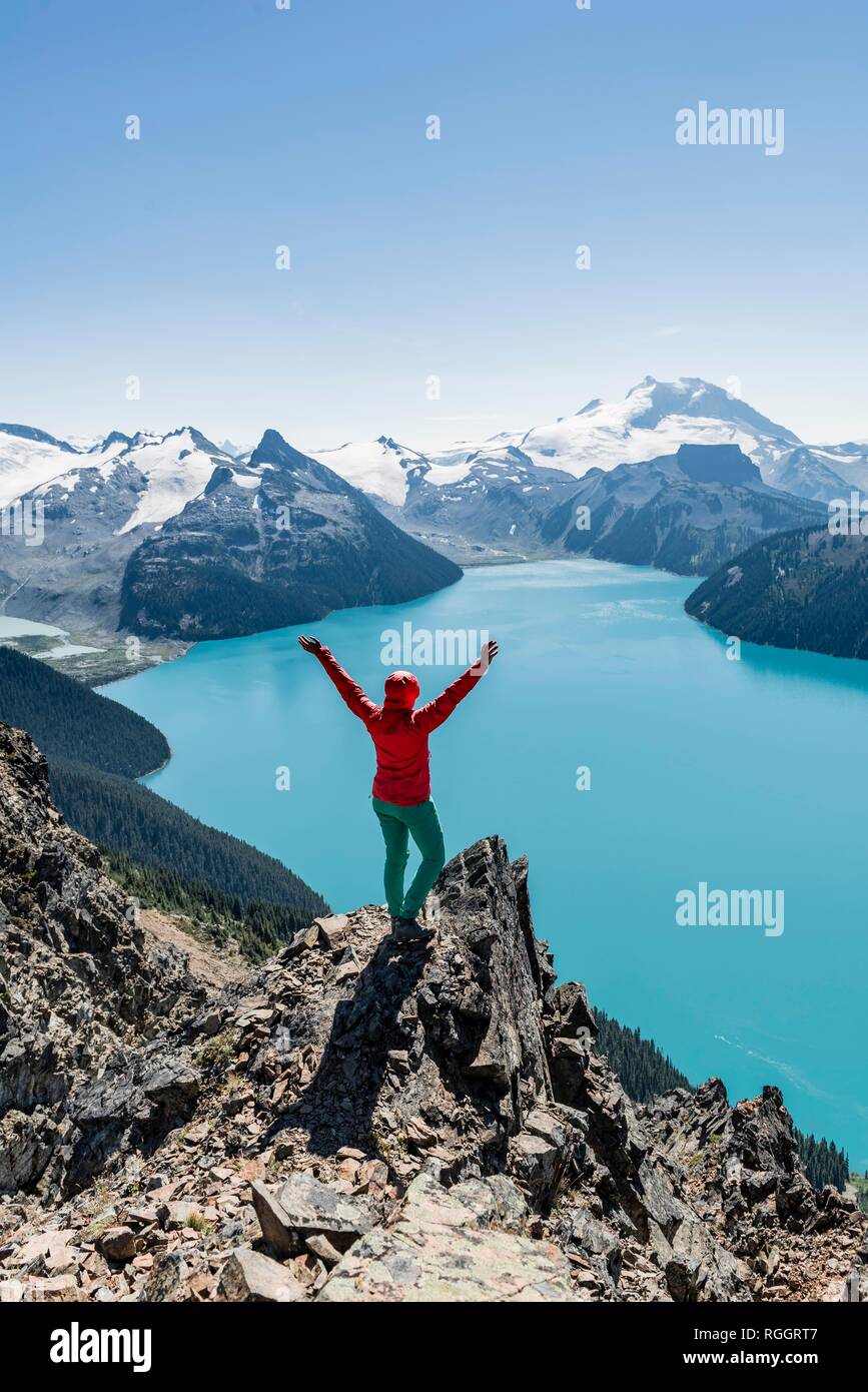 Vista dal crinale panoramico sentiero escursionistico, Escursionista su una roccia si allunga braccia in aria, Lago di Garibaldi, turchese Lago glaciale, Foto Stock