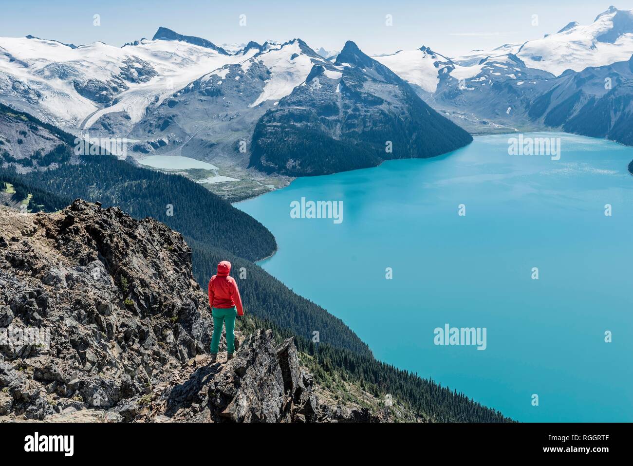 Vista dal crinale panoramico sentiero escursionistico, Escursionista su una roccia, Garibaldi lago, montagna di guardia e inganno di picco, ghiacciaio indietro Foto Stock