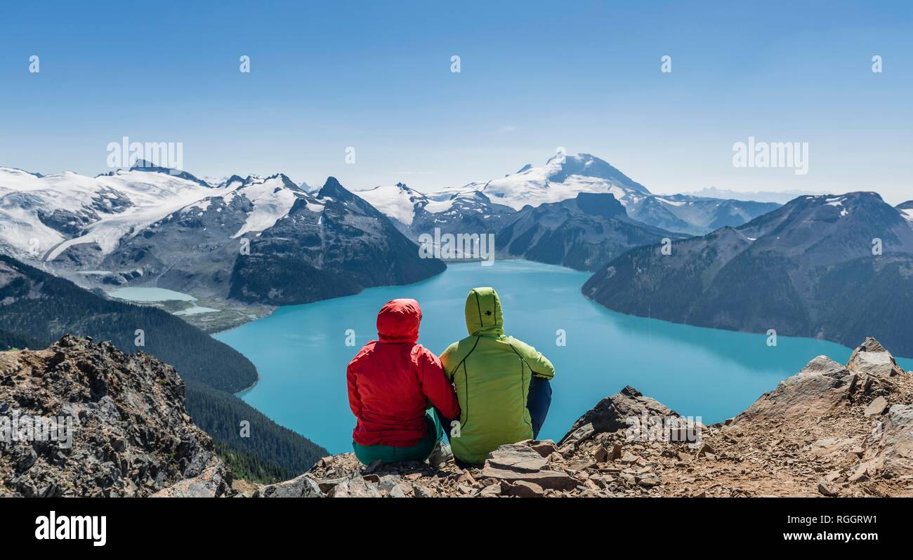 Vista dal panorama Ridge trail, due escursionisti seduto su una roccia con il lago di Garibaldi, turchese lago glaciale, di guardia e di montagna Foto Stock