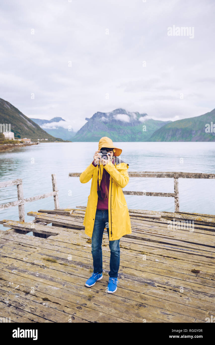 Norvegia, Senja, uomo in piedi su un molo sgangherato presso la costa di scattare una foto Foto Stock