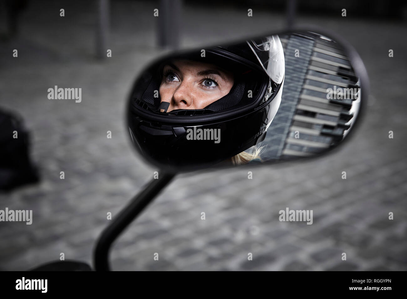 Giovane donna che indossa il casco del motociclo riflessa in specchietto laterale di un motociclo Foto Stock