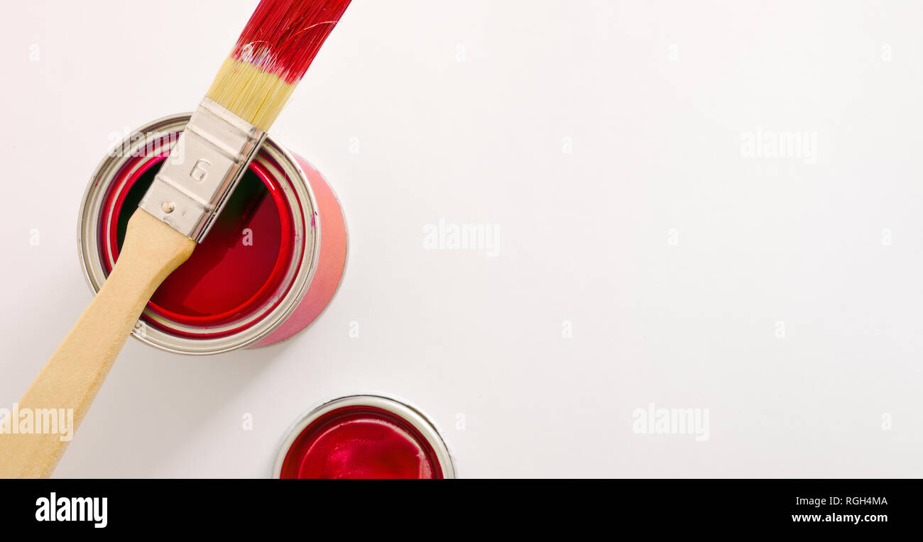 Aprire acrilico rosso barattolo di vernice sul tavolo bianco e il pennello sul pot. Sfondo concettuale del materiale di verniciatura con spazio per il testo. Compo orizzontale Foto Stock