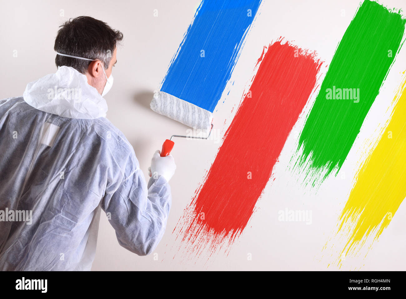 Lo sfondo con il pittore professionista con tute da lavoro e il rullo sul retro di un muro bianco verniciato con quattro colori. Composizione orizzontale. Foto Stock