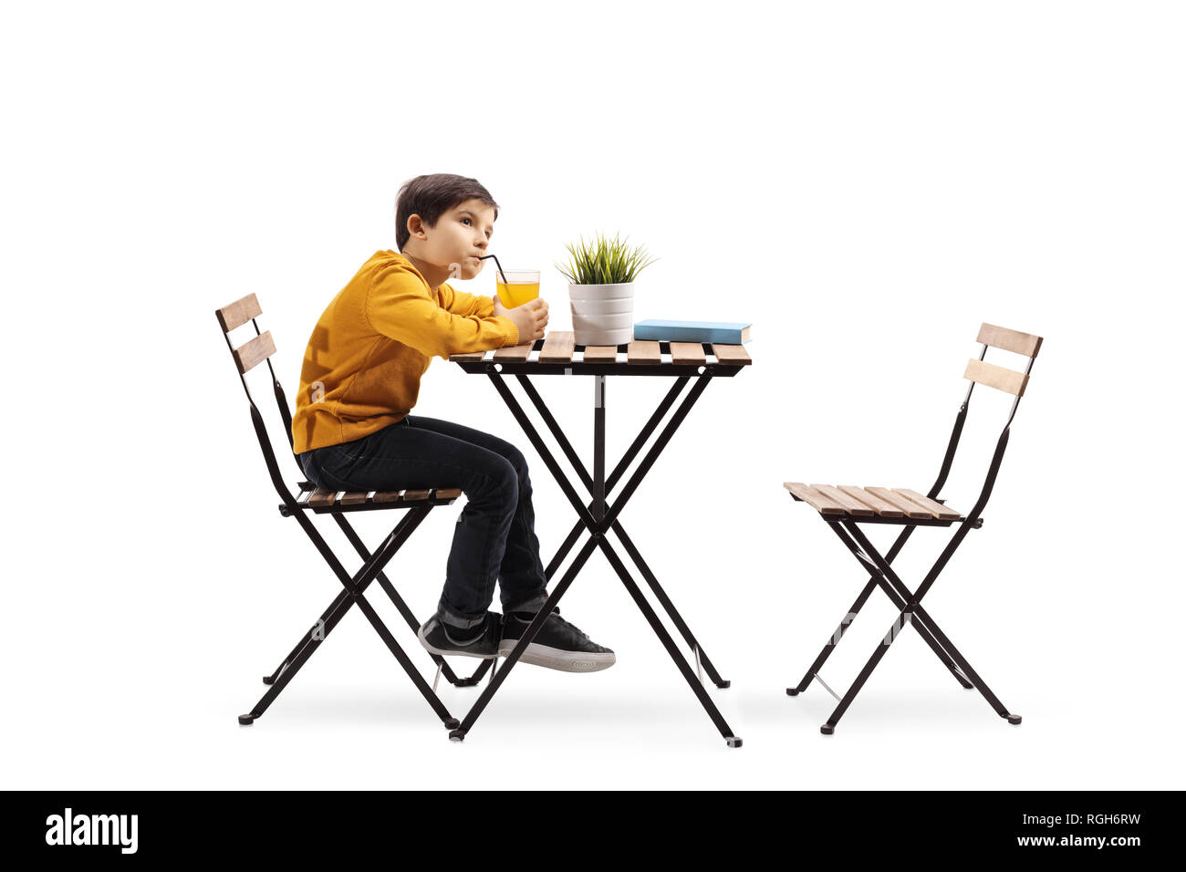 A piena lunghezza shot di un ragazzino di bere succo di frutta e seduto da solo ad un tavolo isolato su sfondo bianco Foto Stock