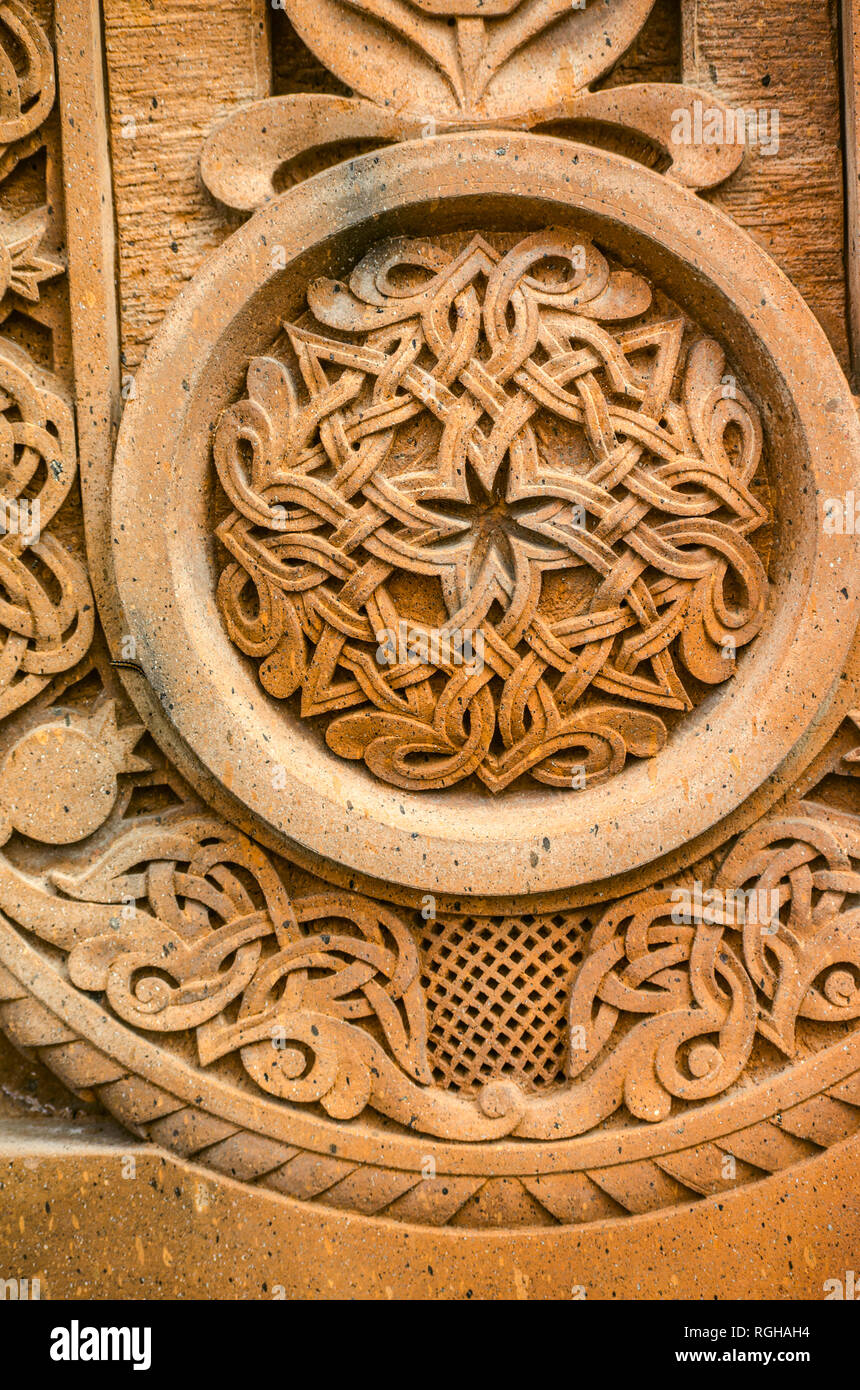 Oshakan,Armenia,19 Februar,2018:scolpito ornamento rotondo con strisce intrecciate di formare un pattern collocato in una cornice rotonda su un rosso di pietra vulcanica Foto Stock
