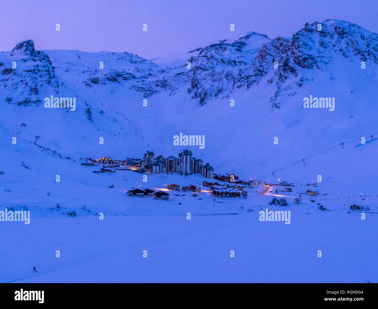 Coperta di neve Tignes Val Claret dal lago al tramonto con il cielo rosa behind blue mountain range con le luci di strada e di una persona che cammina cane sul lago Foto Stock