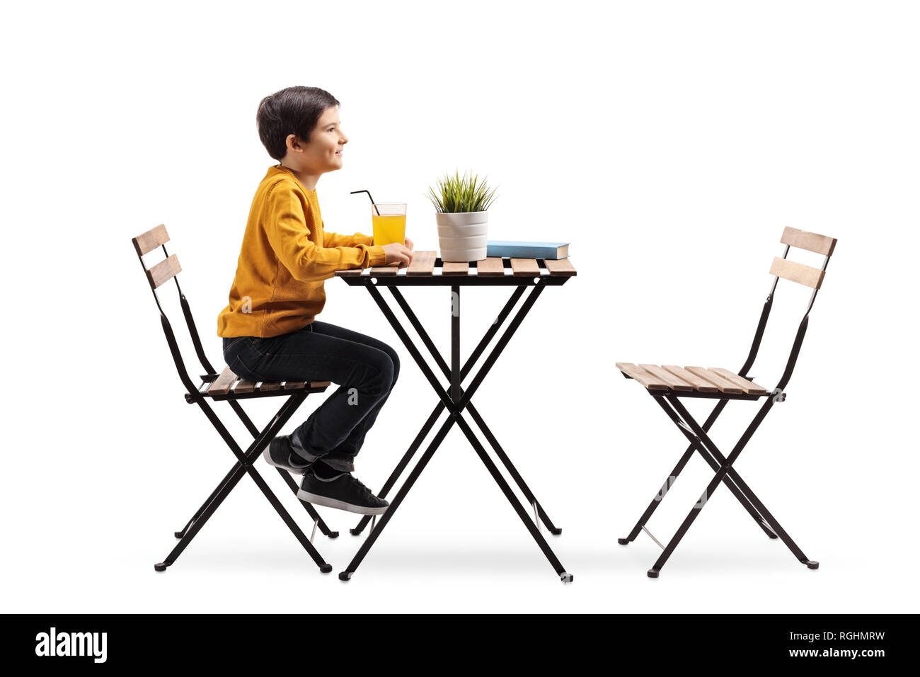Lunghezza piena ripresa di profilo di un piccolo ragazzo seduto da solo a un tavolo con succo di arancia isolati su sfondo bianco Foto Stock