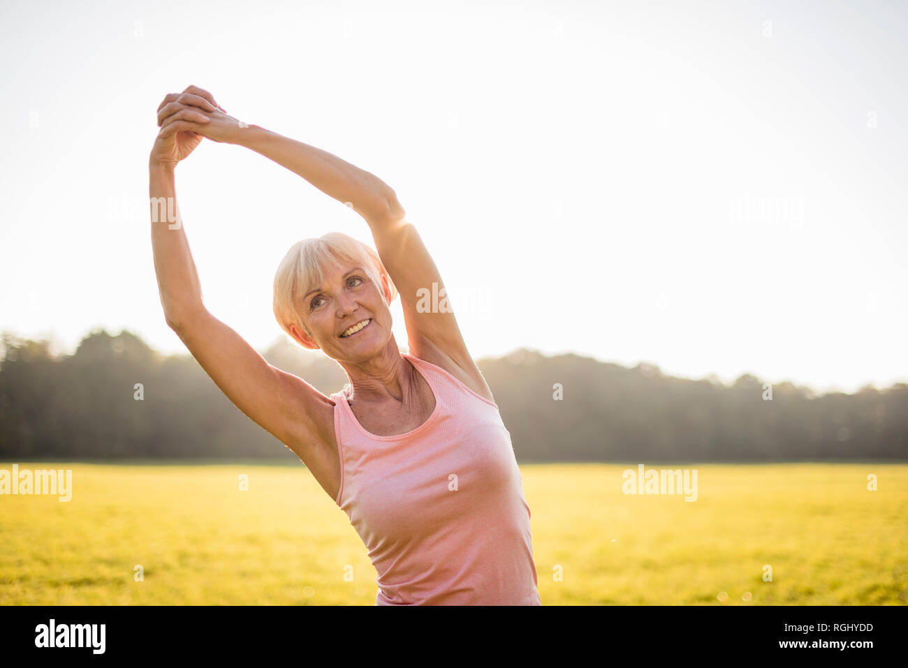 Senior donna stretching sul prato rurale al tramonto Foto Stock