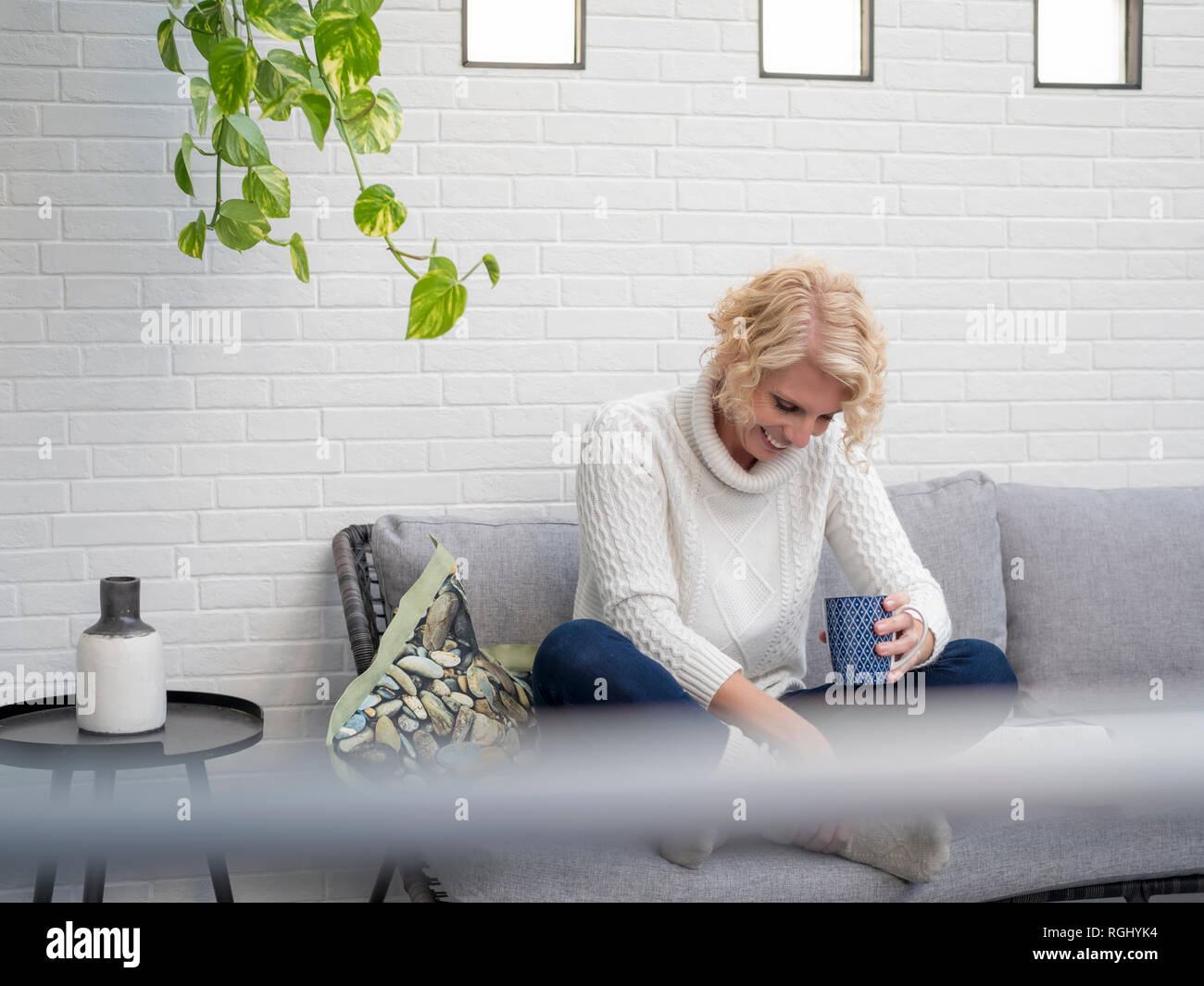 Sorridente donna matura seduti sul divano di casa azienda tazza da caffè Foto Stock