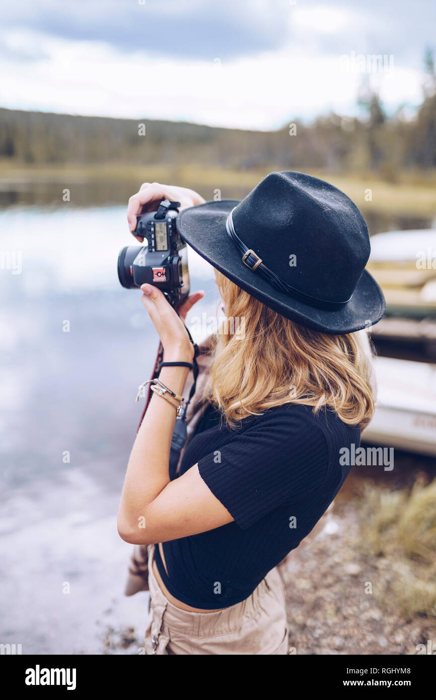 La Svezia, Lapponia, giovane donna vestita di nero hat tenendo la foto con la fotocamera Foto Stock