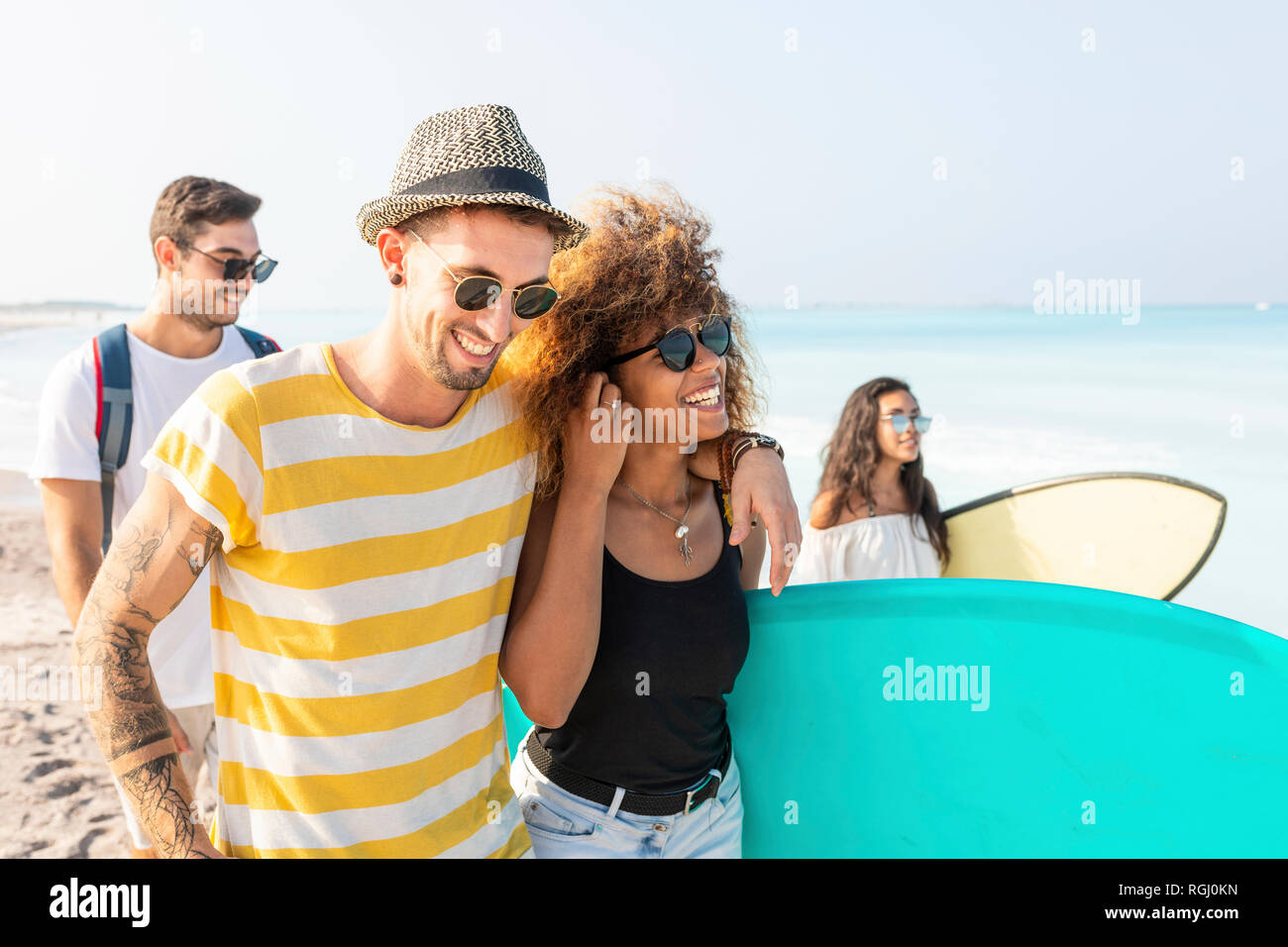 Gruppo di amici di camminare sulla spiaggia, portando le tavole da surf Foto Stock