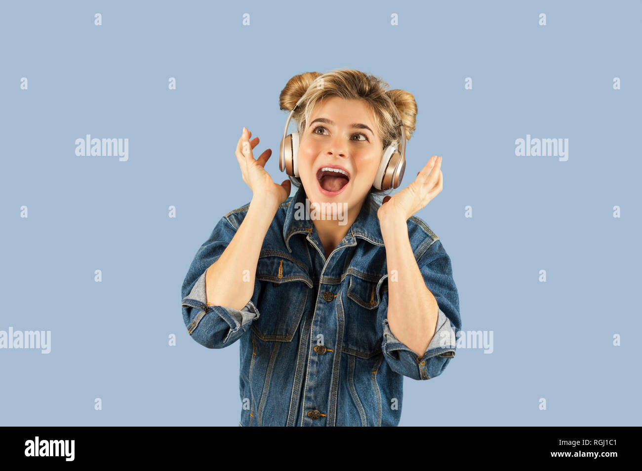 Affascinante giovane bella ragazza nelle cuffie canta e danza in studio isolato su un fondo blu. Concetto di felicità della vita musicale Foto Stock