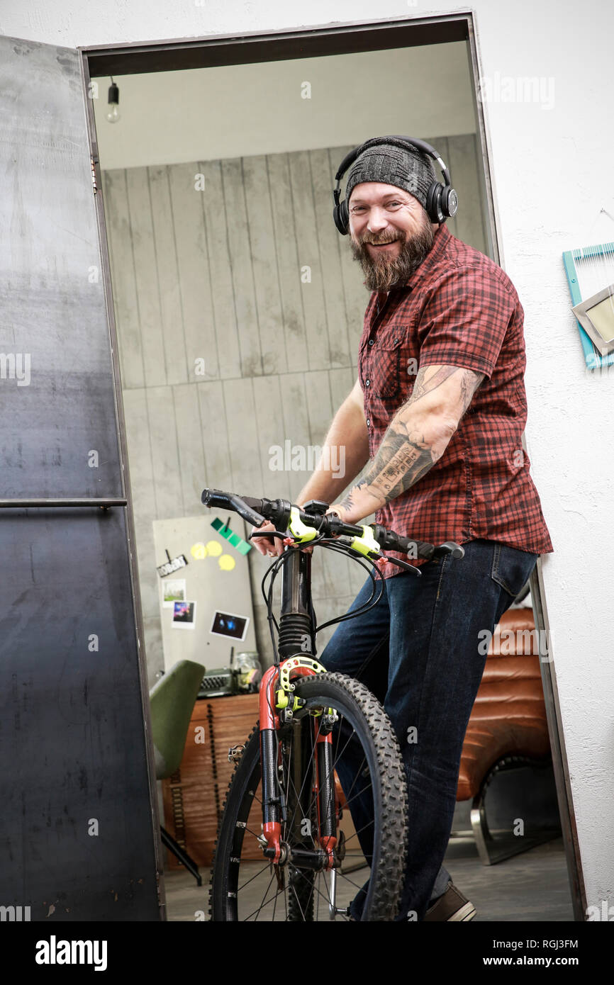 Ritratto di uomo felice con la bicicletta che indossano le cuffie in ufficio Foto Stock