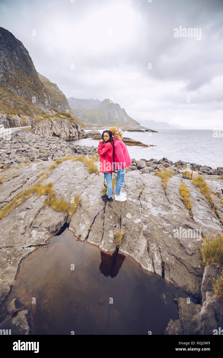 Norvegia Lofoten, due donne che indossano rainjackets in piedi di schiena su una roccia Foto Stock