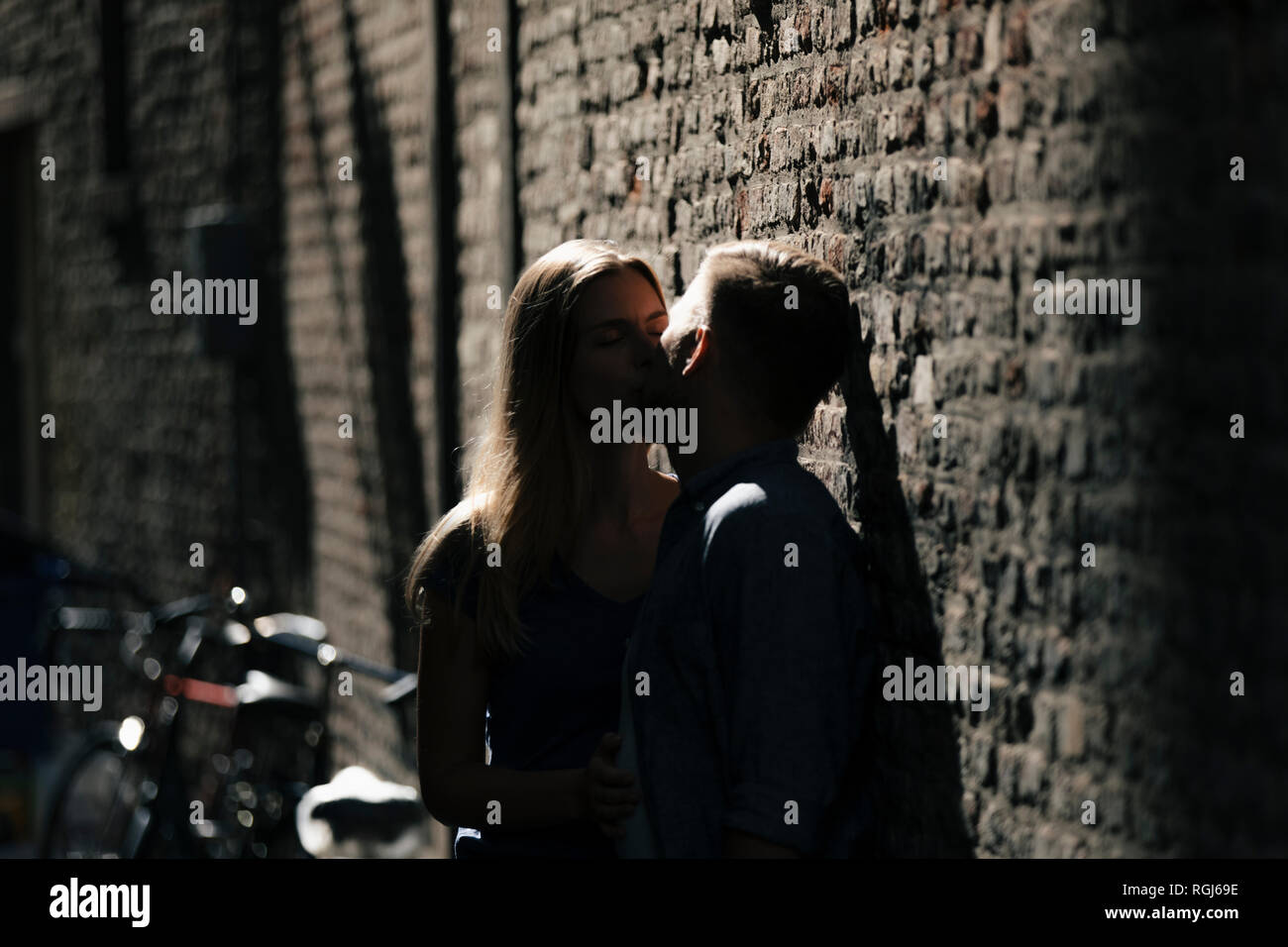 Affettuosa coppia giovane kissing in corrispondenza di un muro di mattoni Foto Stock