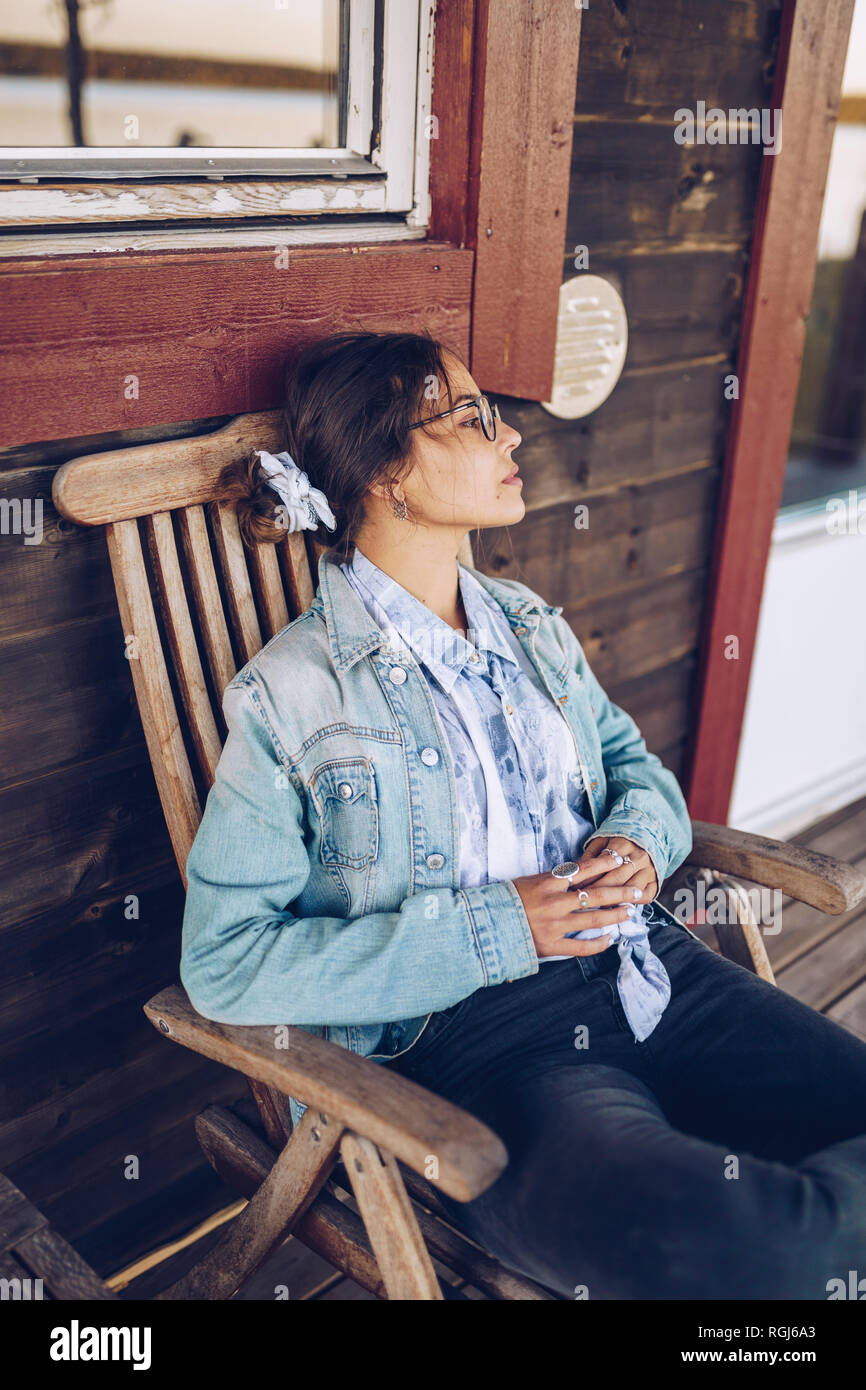 La Svezia, Lapponia, pensieroso giovane donna seduta su una sedia sulla veranda che guarda a distanza Foto Stock