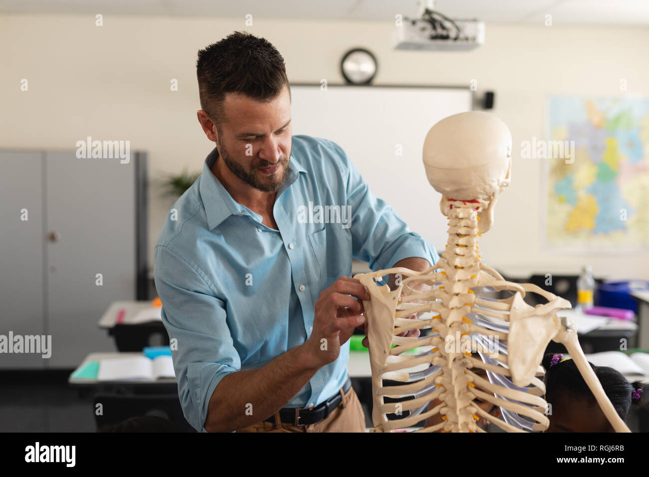 Insegnante di sesso maschile che fissa il modello dello scheletro in aula Foto Stock