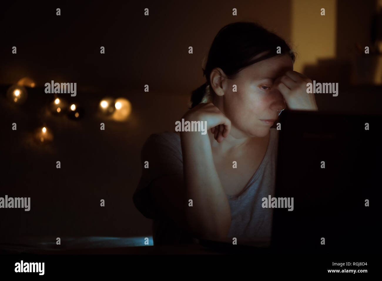 Stanco della donna lavoro straordinario sul computer portatile durante la notte nel suo ufficio a casa, viso è illuminato dalla luce blu dello schermo Foto Stock
