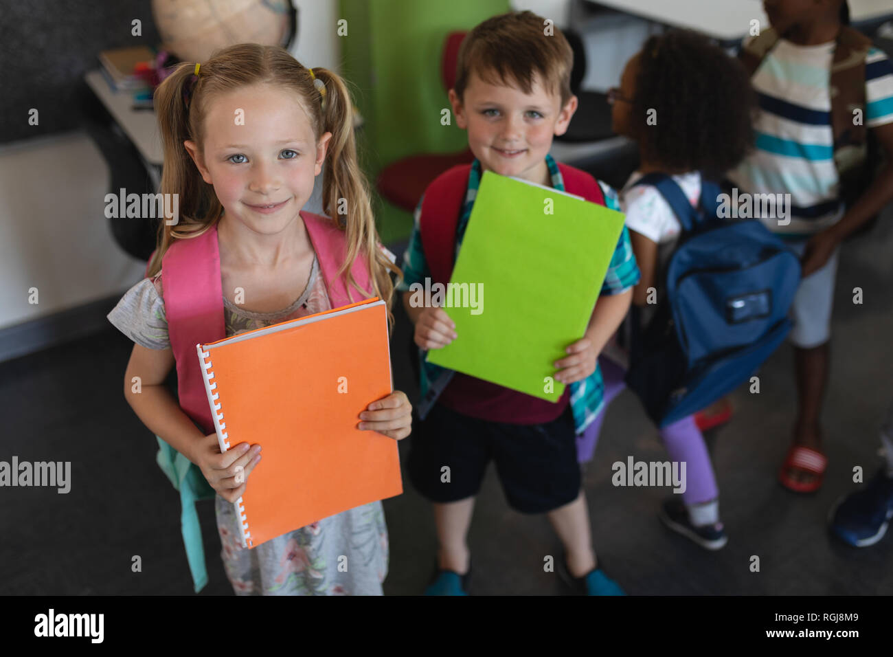 Vista frontale della holding schoolkid notebook e guardando la telecamera in aula Foto Stock