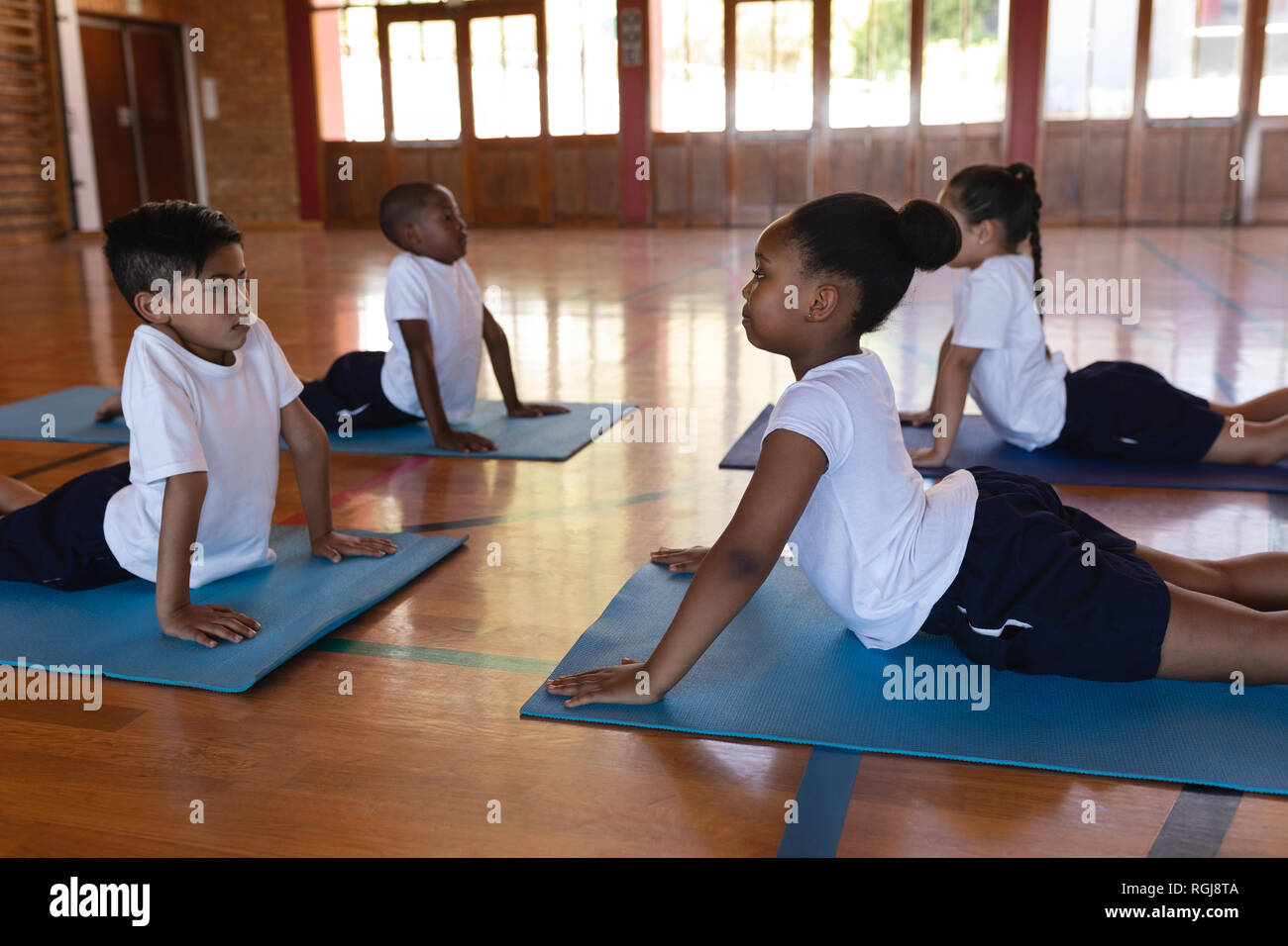 Schoolkids fare yoga su un materassino yoga nella scuola Foto Stock