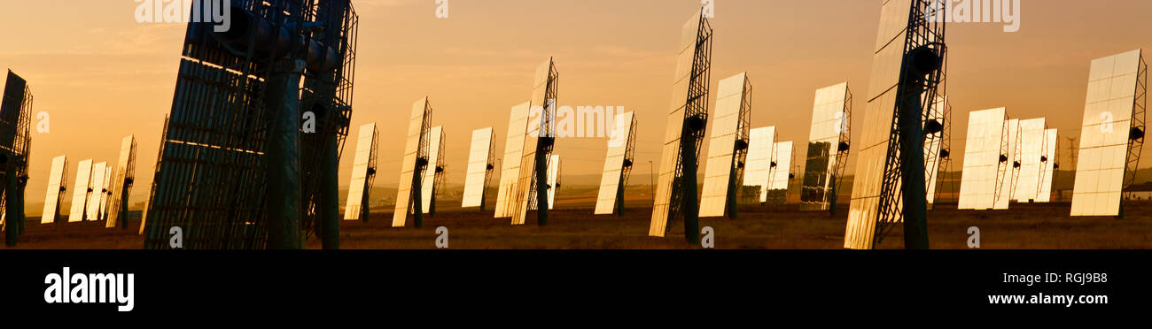 Panoramica banner web campo di energia solare dei pannelli a specchio sfruttando i raggi del sole per fornire alternative di energia verde all'alba o al tramonto Foto Stock
