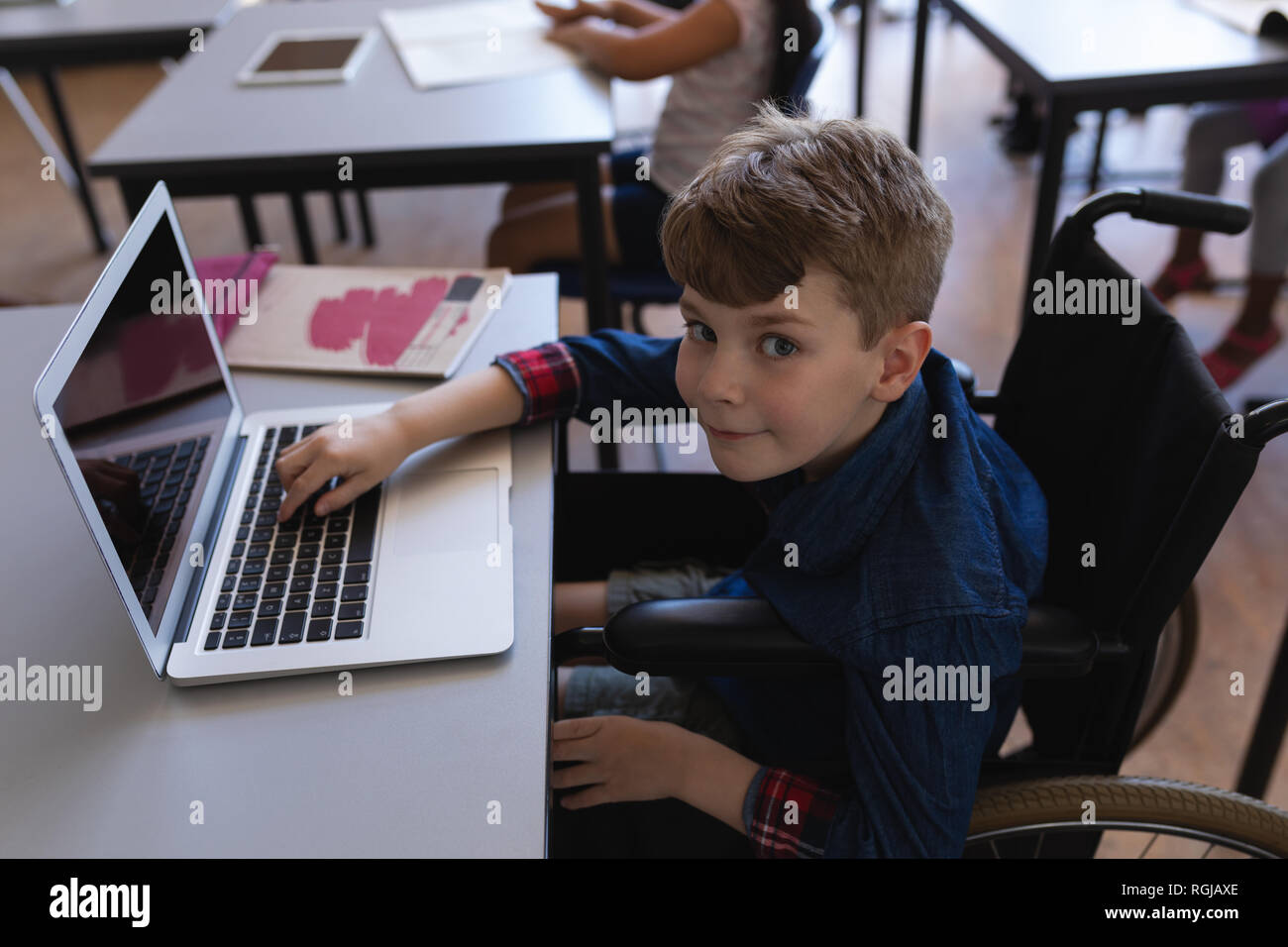 Disattivare schoolboy studiando su laptop mentre è seduto alla scrivania in aula Foto Stock