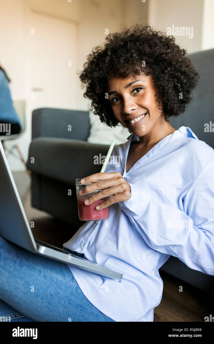 Ritratto di donna sorridente con soft drink seduti sul pavimento con il computer portatile Foto Stock