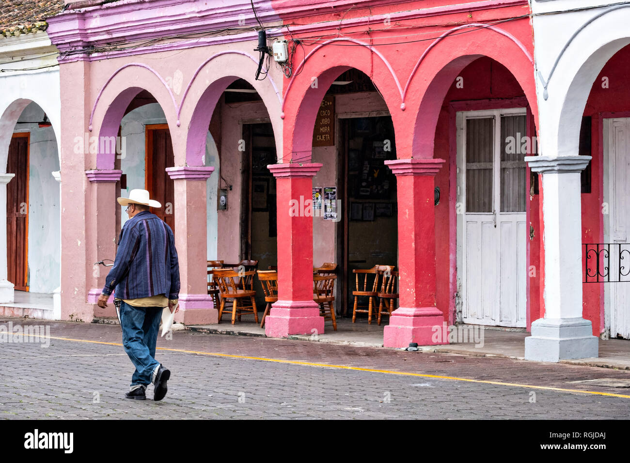 Un uomo cammina passato un colonnato variopinto edificio di stile in Tlacotalpan, Veracruz, Messico. La piccola città è dipinto un tripudio di colori e le caratteristiche ben conservate Caraibi coloniale stile architettonico risalente alla metà del XVI ° secolo. Foto Stock