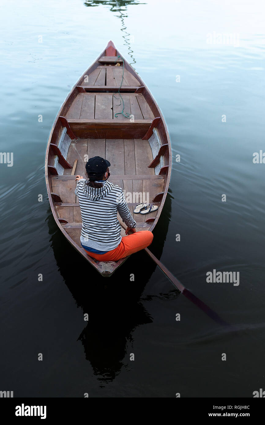 Un solitario righe femmina la sua riga di legno barca nella calma acqua liscia dal buio al bianco. Foto Stock Un solitario righe femmina la sua riga di legno barca nella calma acqua liscia dal buio al bianco. Foto Stock