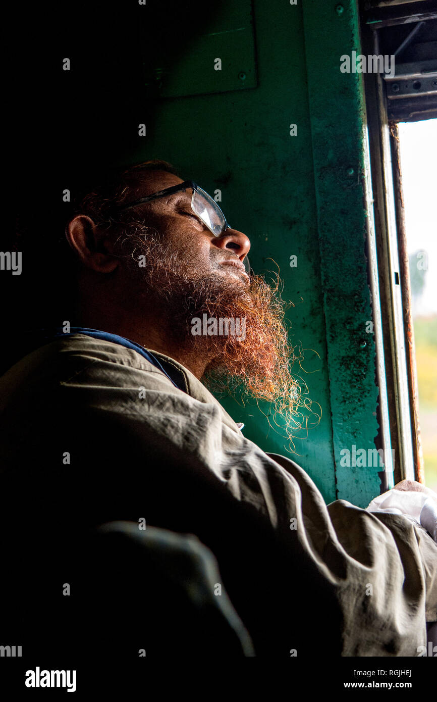 Un uomo asiatico con un rosso ispido barba dal Myanmar prende un pisolino su un lungo viaggio in treno Foto Stock