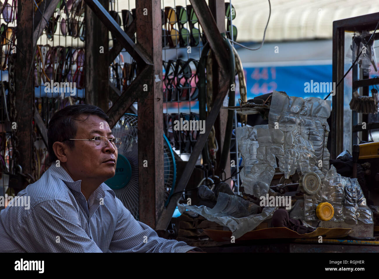 Un locale di mezza età uomo asiatico si siede al suo lato strada rendendo chiave in stallo in attesa di scambi di Phnom Phen, Cambogia. Foto Stock
