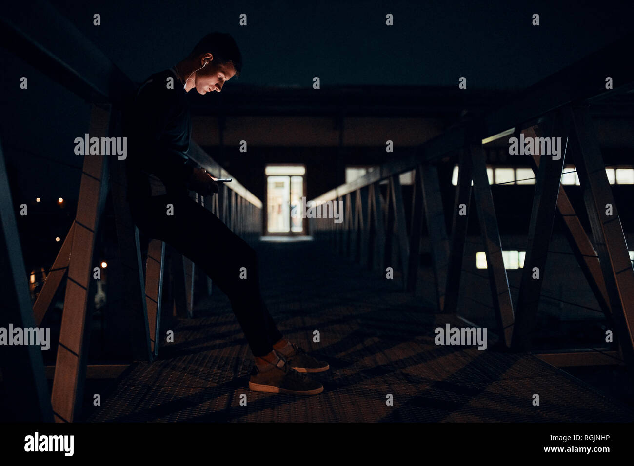 Attività sportive giovane uomo con lo smartphone e gli auricolari in piedi su un ponte di notte Foto Stock
