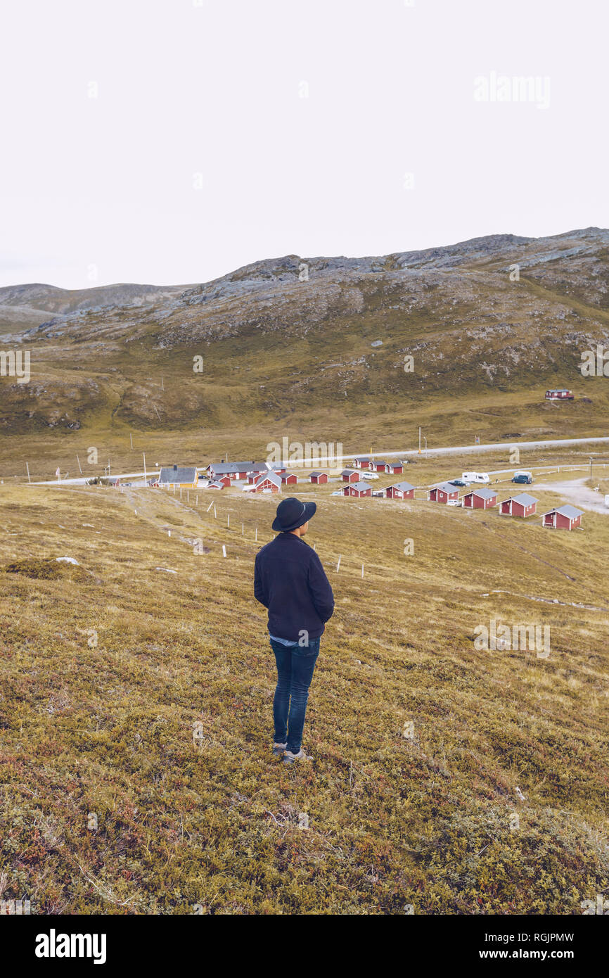 Giovane uomo in piedi su una collina, lookig su un insediamento, Capo Nord, Norvegia Foto Stock