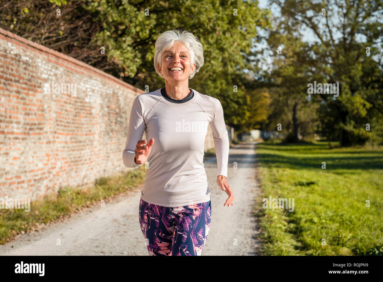 Felice senior donna che corre lungo un muro di mattoni in un parco Foto Stock