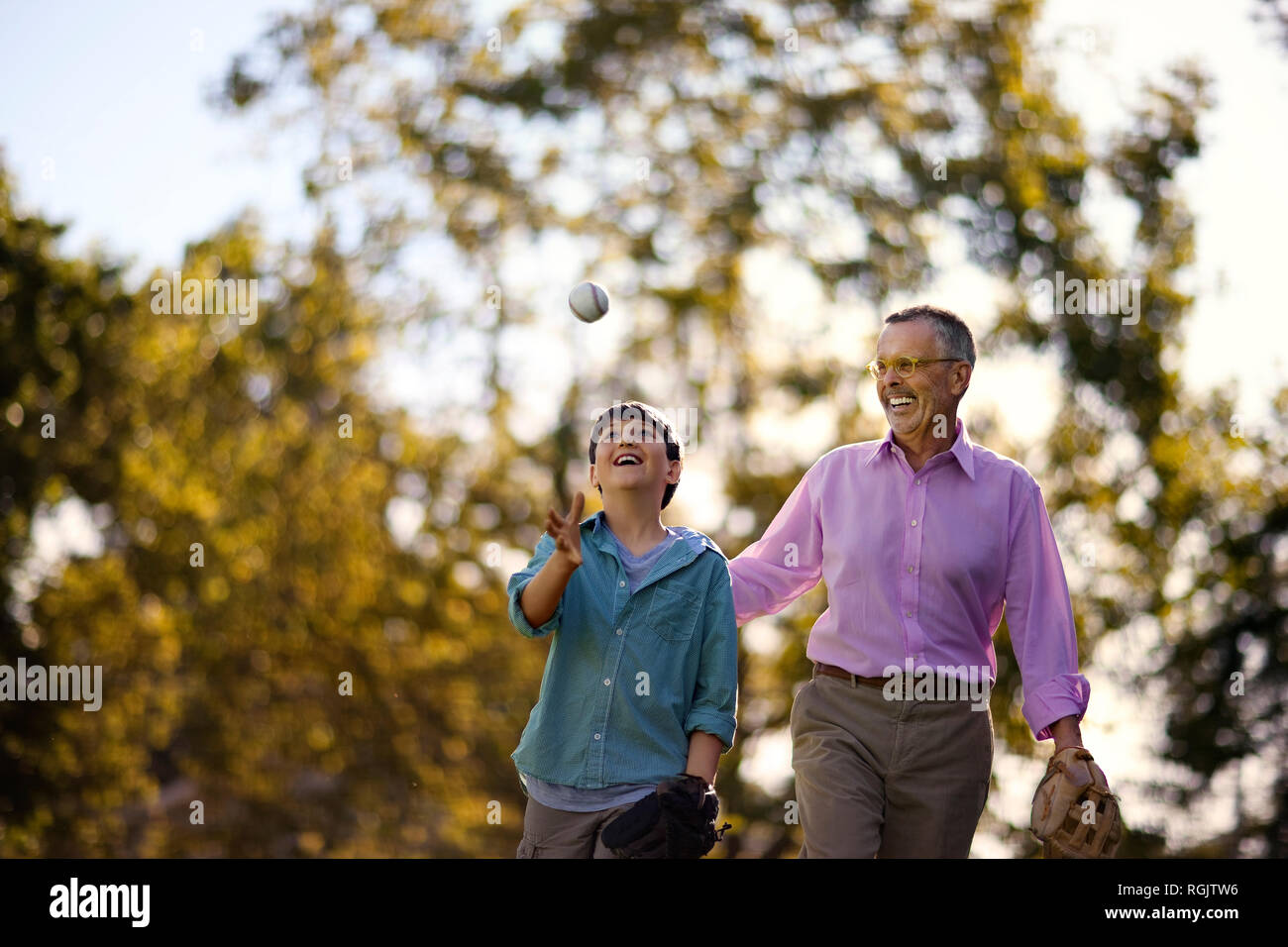 Ridendo uomo maturo guardando suo Figlio lanciare una palla da baseball in aria come essi a piedi attraverso un parco insieme. Foto Stock