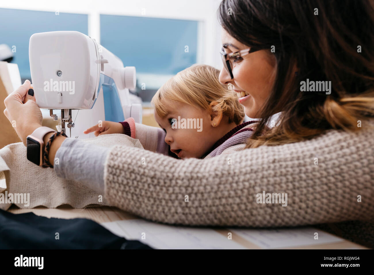 Felice madre con piccola figlia a casa utilizzando la macchina per cucire Foto Stock