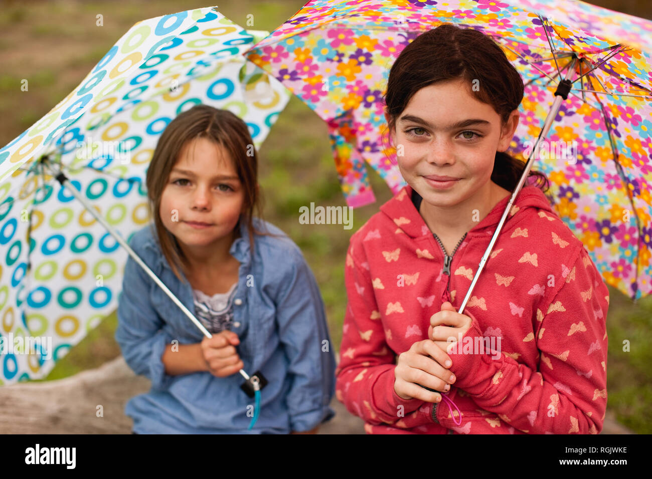 Due giovani ragazze a sedersi su un albero caduto tronco tenendo ombrelli aperti come hanno sorriso e posare per un ritratto. Foto Stock