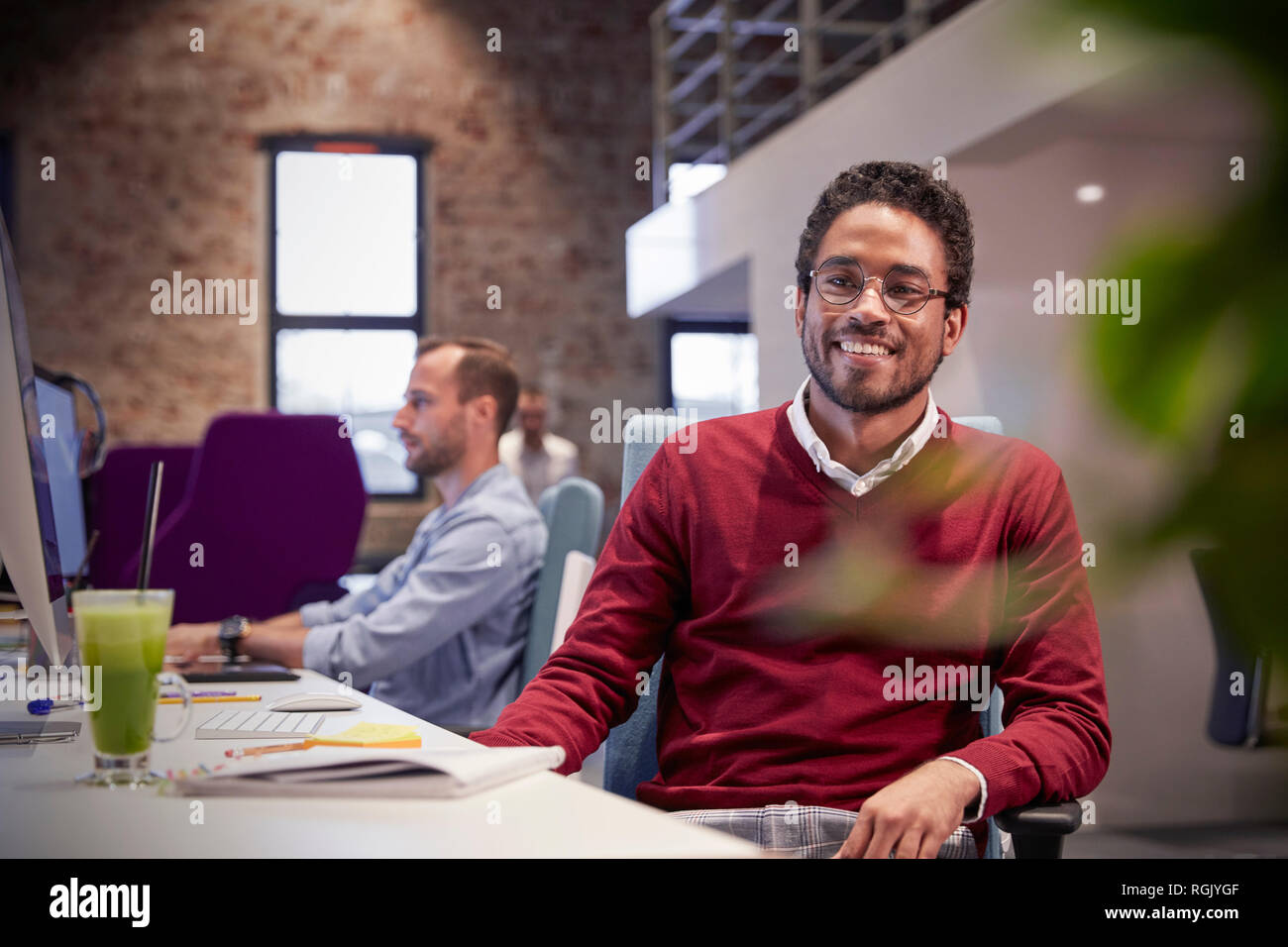 Giovane uomo seduto alla scrivania in ufficio, sorridente Foto Stock