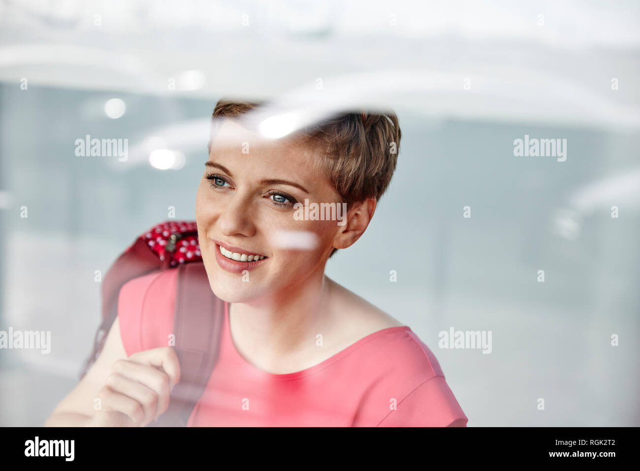 Ritratto di donna sorridente con zaino dietro il vetro di finestra Foto Stock