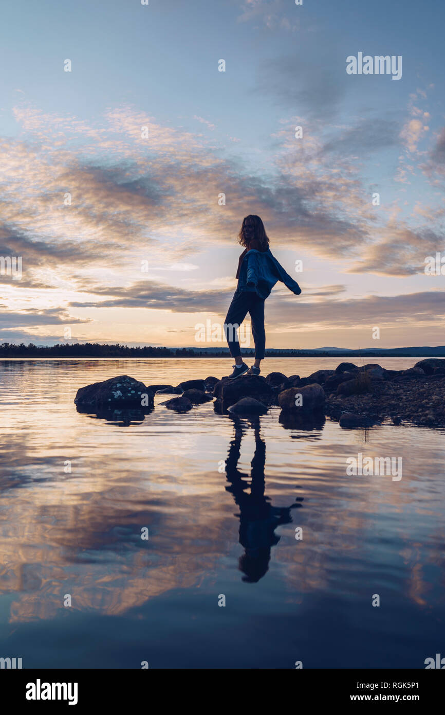 Giovane donna in piedi al lago Inari, con le braccia aperte, Finlandia Foto Stock