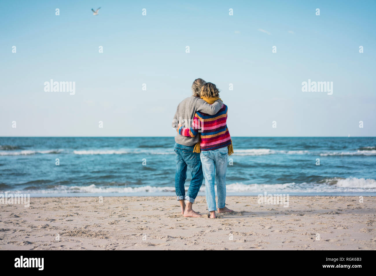 Ture giovane permanente sulla spiaggia con bracci intorno, guardando il mare Foto Stock