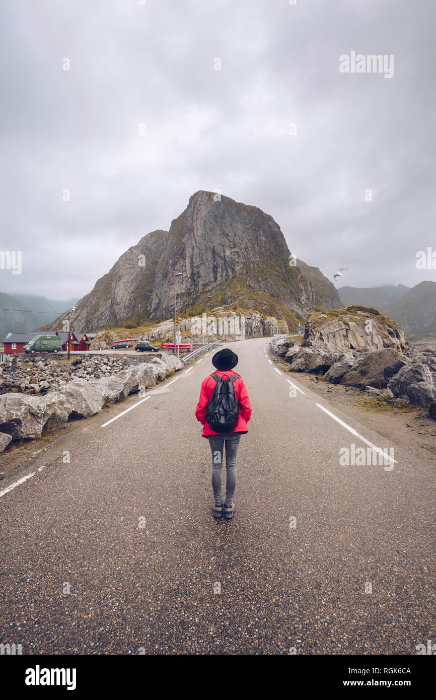 Norvegia Lofoten, Hamnoy, vista posteriore dell'uomo con zaino in piedi sulla strada vuota Foto Stock