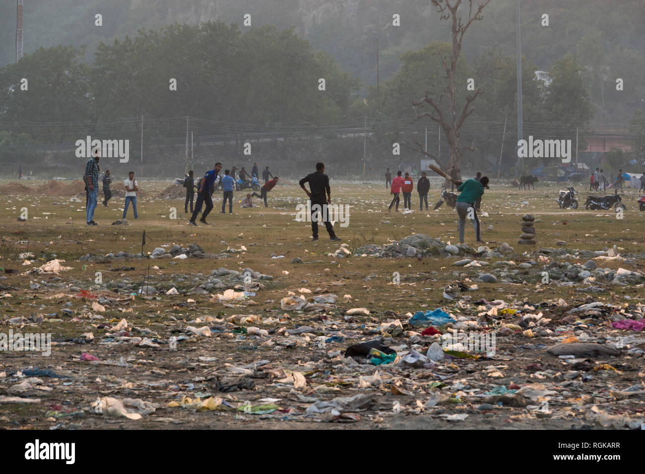Giovani uomini gioco di cricket tra immondizia di plastica e di altri rifiuti in Haridwar, India Foto Stock