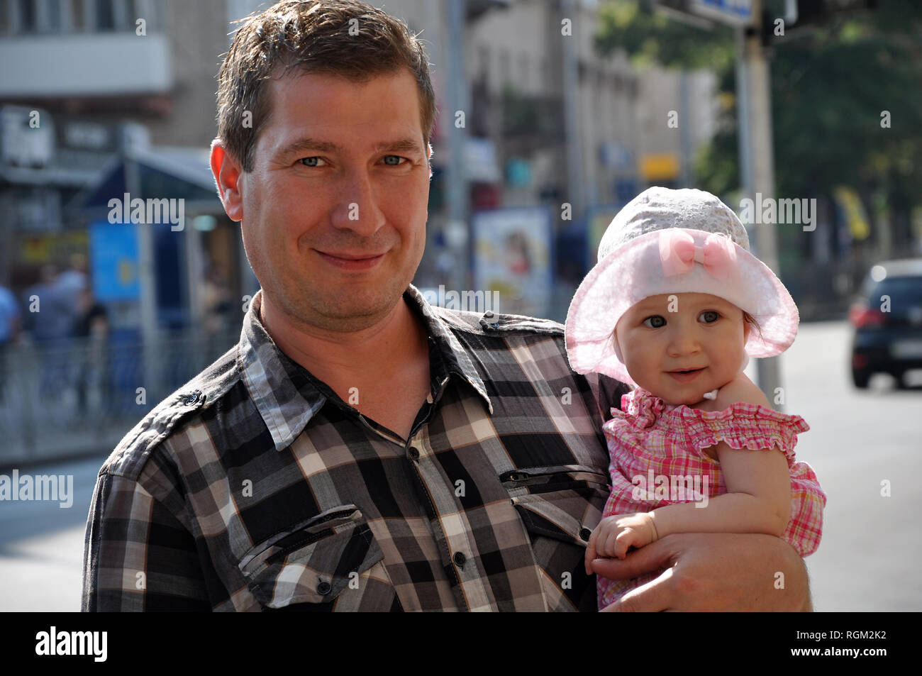 Ritratto di Padre sorridente e la sua bimba in un plaid vestiti su una offuscata Estate Città sullo sfondo di strada Foto Stock