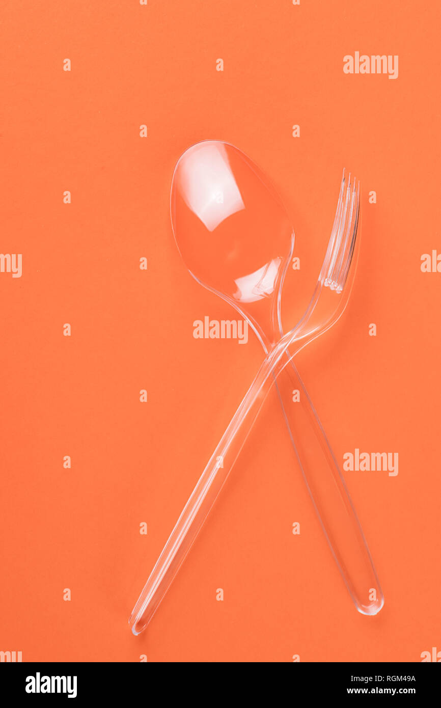In plastica trasparente cucchiaio e forchetta su sfondo arancione vista superiore Foto Stock