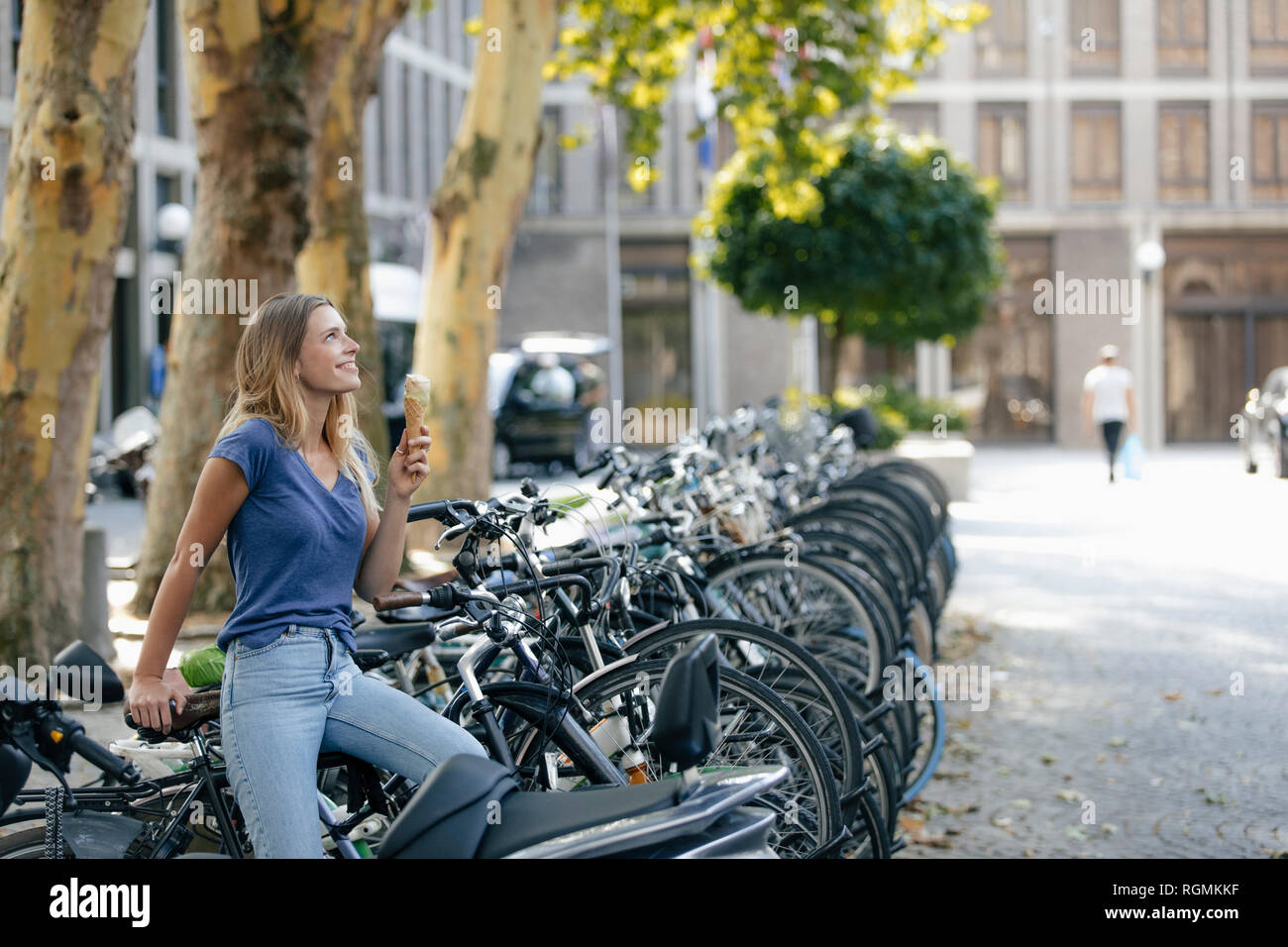 Paesi Bassi, Maastricht, sorridente ragazza bionda tenendo cono gelato in città al rack per bicicletta Foto Stock
