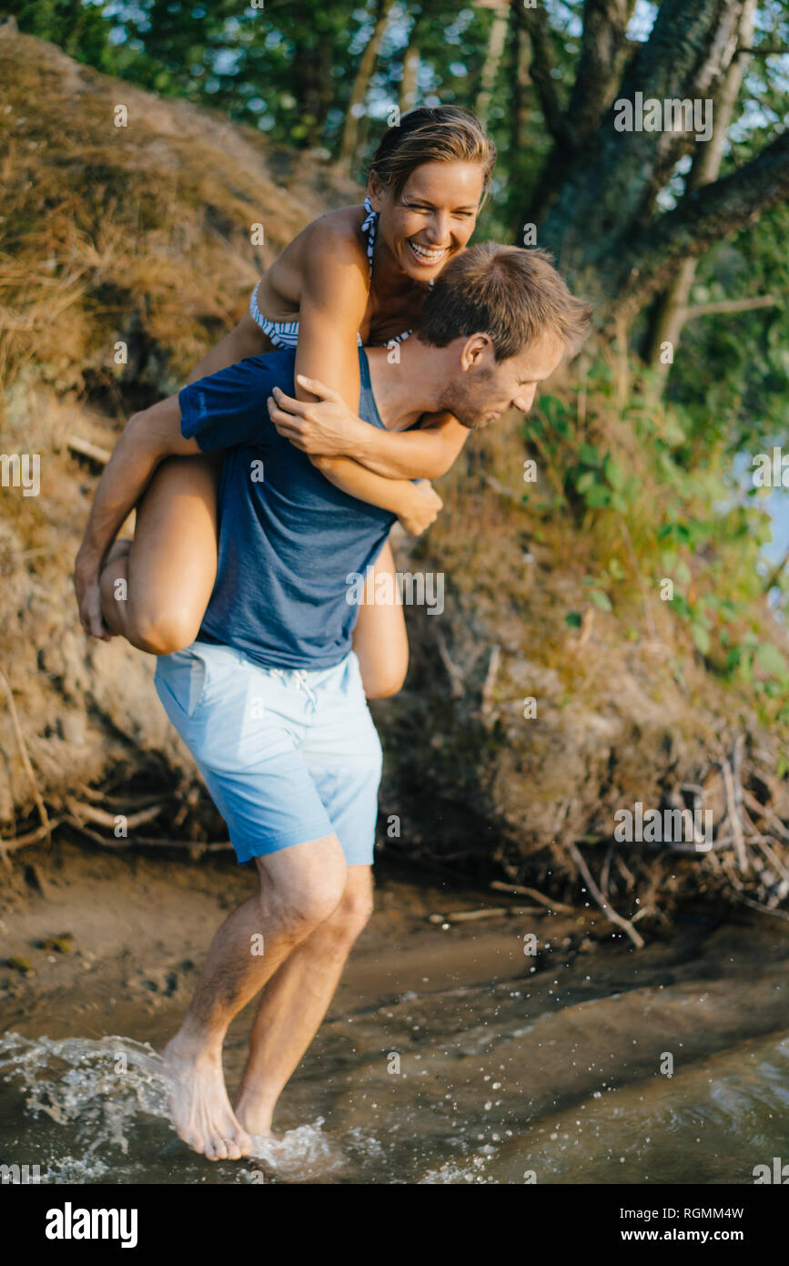 Felice l'uomo che porta la fidanzata sovrapponibile a un lago Foto Stock