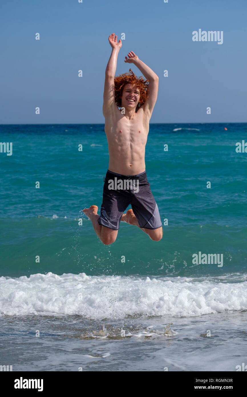 Ritratto di redheaded giovane uomo di saltare in aria a seashore Foto Stock